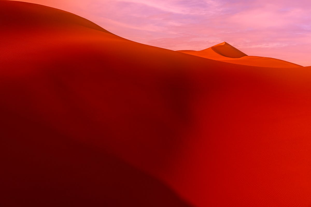 Soft red dunes flowing beneath a pink sky - the yielding, shape-shifting quality of over-giving